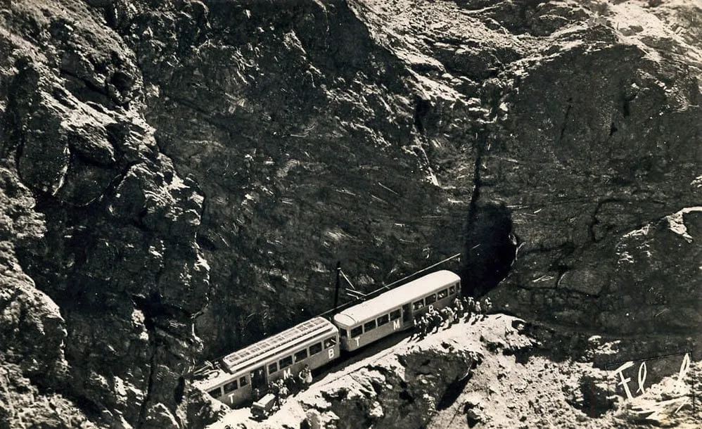 Photo d'archive : deux automotrices du Tramway du Mont-Blanc à l'arrêt sur le flanc rocheux, des voyageurs descendus le long de la voie
